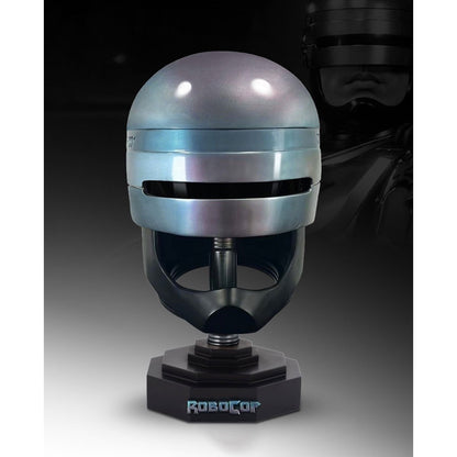 A RoboCop helmet display stand featuring a metallic silver and blue helmet replica on a black base with the 'RoboCop' logo, set against a dark background with a faint character silhouette.